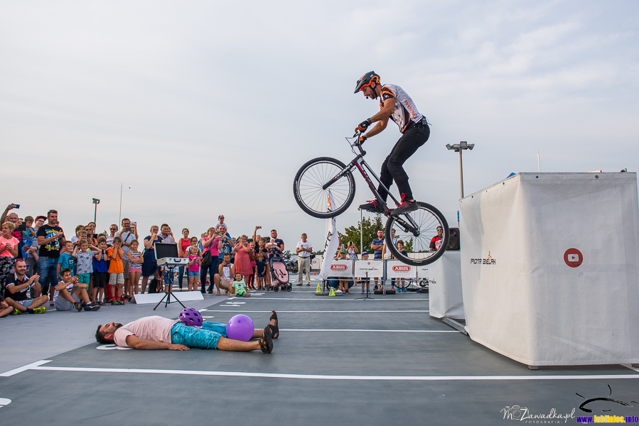 pokaz sztuczek na rowerze - Piotr Bielak; skok z wysokości na leżącego na ziemi mężczyznę, pomiędzy nogami balon, który zostanie przebity przez skaczącego artystę