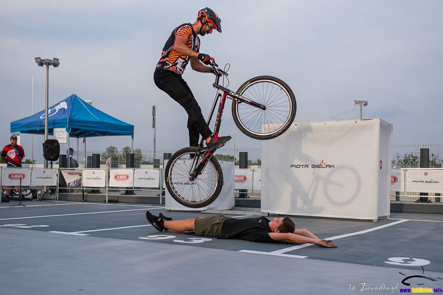 pokaz sztuczek na rowerze - Piotr Bielak; przeskoki nad leżącym na ziemi uczestnikiem pokazu