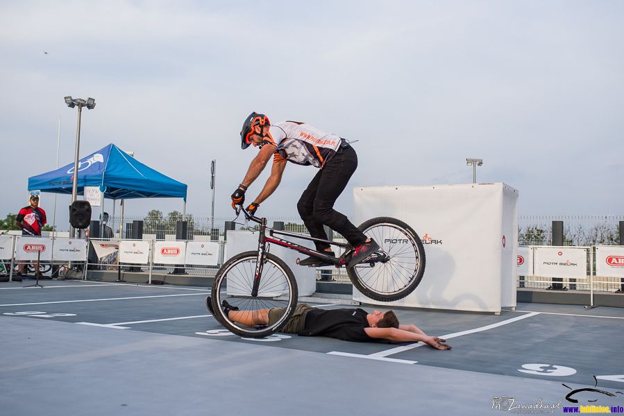 pokaz sztuczek na rowerze - Piotr Bielak; przeskoki nad leżącym na ziemi uczestnikiem pokazu